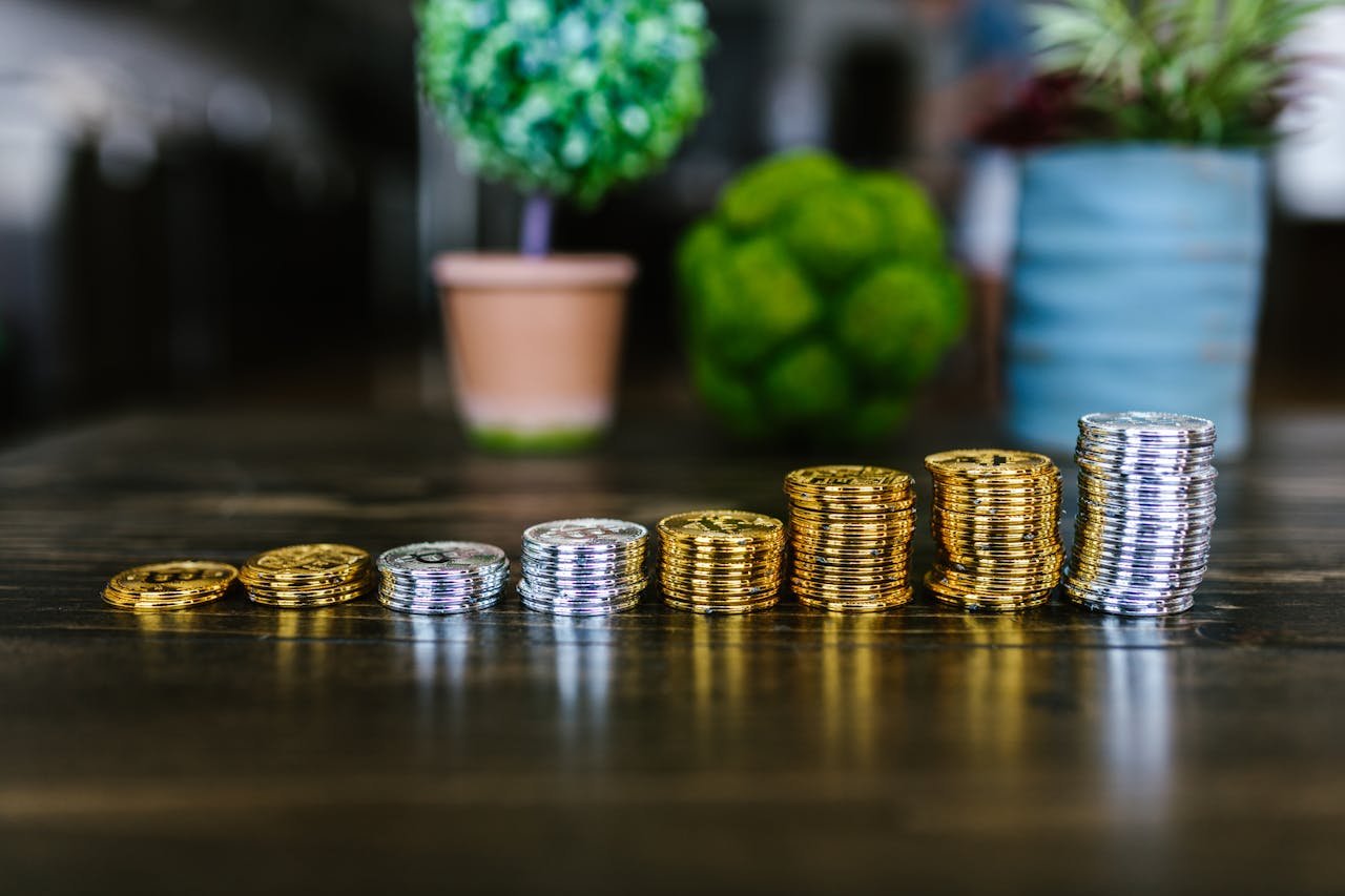 services-04 Close-up of stacked gold and silver bitcoins on a wooden table with plants in the background.